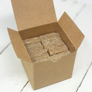 May include: A brown cardboard box with the lid open, revealing a stack of rectangular bars of soap. The soap is a light brown color and has a rough texture.