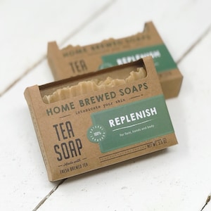 May include: Two boxes of tea soap are displayed, each with a natural kraft paper design. The front box features the text "TEA SOAP" and "REPLENISH" on a green label. The soap is 3.5 oz.