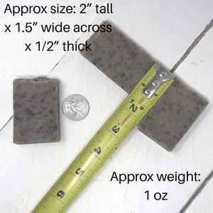 May include: Two bars of speckled grey soap, one measured with a yellow tape measure. The soap is 2 inches tall, 1.5 inches wide, and 1/2 inch thick. The text reads "Approx size: 2" tall x 1.5" wide across x 1/2" thick" and "Approx weight: 1 oz".