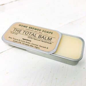 Puede incluir: Una peque&ntilde;a lata de plata con una etiqueta marr&oacute;n que dice "HOME BREWED SOAPS THE TOTAL BALM 0.25 OZ 100% Natural Handmade Ingredients: Shea, Tucama & Cocoa Butter. Coconut, Avocado & Jojoba Oils. Carnauba Wax. Vegan."