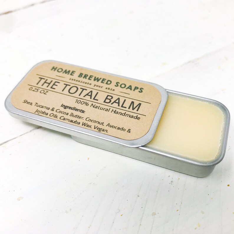 Puede incluir: Una peque&ntilde;a lata de plata con una etiqueta marr&oacute;n que dice "HOME BREWED SOAPS THE TOTAL BALM 0.25 OZ 100% Natural Handmade Ingredients: Shea, Tucama & Cocoa Butter. Coconut, Avocado & Jojoba Oils. Carnauba Wax. Vegan."