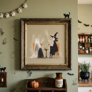 May include: A framed print depicts a ghost and a witch enjoying coffee, set against a light green wall adorned with Halloween-themed decorations. A small pumpkin and a jar labeled "Dragon's Breath" sit on a wooden shelf below the artwork. A string of ghost-shaped lights hangs above.