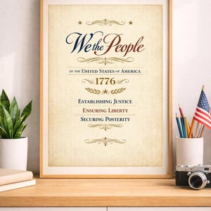 Op de afbeelding: Ingelijste print met de tekst "We the People" in elegant schrift, met het jaar 1776 en de zinnen "Establishing Justice, Ensuring Liberty, Securing Posterity". De print heeft een vintage perkament achtergrond en wordt weergegeven op een houten oppervlak.