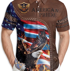 May include: Brown polo shirt with an American flag and eagle design. The shirt features the text "AMERICAN PRIDE" and a patriotic emblem. The design incorporates the colors red, white, and blue.
