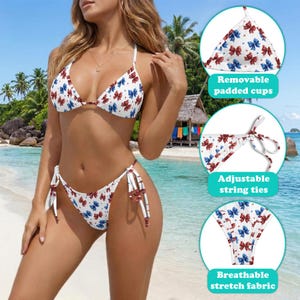 May include: A white bikini set featuring a repeating pattern of small red and blue bows. The top includes removable padded cups, and the bottom features adjustable string ties on the sides. The fabric is described as breathable and stretchable.