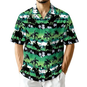 May include: Short-sleeved button-down shirt with a green and white tropical design. The shirt features black silhouettes of cowboys riding bulls, palm trees, and floral accents. The shirt has a classic collar and a relaxed fit.