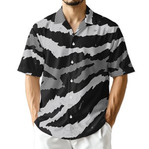 May include: Short-sleeved button-down shirt with a black and gray zebra stripe pattern. The shirt has a classic collar and white buttons. The design features bold, irregular stripes, creating a striking visual effect. The shirt is a casual wear item.