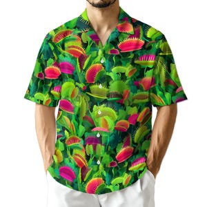 May include: Short-sleeved button-down shirt with a vibrant all-over print of Venus flytraps. The shirt features a dark green background with bright green, pink, and red carnivorous plants. The collar and buttons are visible, and the shirt is worn by a person.