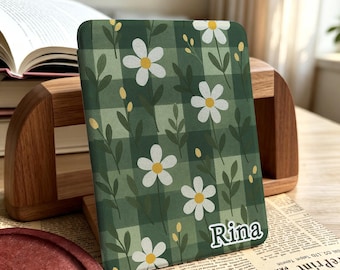 Pode incluir: Uma capa retangular para leitor de e-books com um padrão xadrez em verde escuro e claro, decorada com flores de margarida brancas, caules verdes e pequenos botões amarelos. O nome Rina está impresso em letras brancas no canto inferior direito.