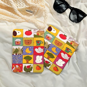 以下が含まれることがあります： クマ、リンゴ、家、その他の気まぐれな要素の漫画イラストを特徴とする、パッチワークデザインの2つのカラフルな模様のケース。ケースはサングラス付きの白い表面にあります。