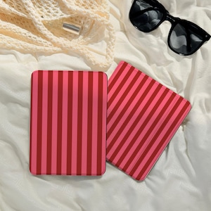 May include: Two rectangular cases with a pink and red striped design. The cases are on a white surface, with black sunglasses and a cream-coloured bag in the background.