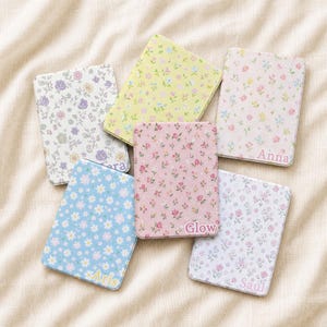 Peut inclure: Six miroirs de poche rectangulaires ornés de divers motifs floraux aux couleurs pastel. Trois miroirs sont personnalisés avec les prénoms Anna, Glow et Saul, tandis qu'un miroir porte le prénom Aris. Chaque miroir a une surface lisse et plate.