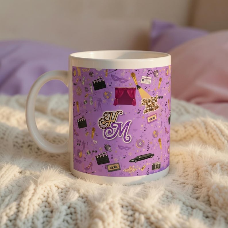 May include: White ceramic mug with a purple background featuring various entertainment-themed icons, including a stage, film clapper, and a limousine. The mug has the initials "HM" in a decorative font and the text "Best of both worlds".