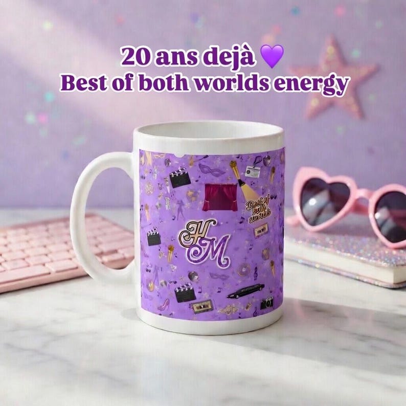 May include: White ceramic mug with a purple pattern featuring film-related icons and the initials "H M". The mug has the text "20 ans d&eacute;j&agrave;" and "Best of both worlds energy". Pink heart-shaped sunglasses and a keyboard are in the background.