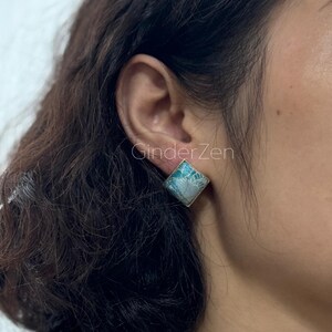 Puede incluir: Pendientes cuadrados con borde plateado y diseño veteado turquesa y blanco. Los pendientes se llevan en la oreja. El texto "GinderZen" es visible en la imagen.