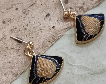 May include: A pair of gold-toned stud earrings. Each earring features a fan-shaped design with a black background, gold-colored center, and blue accents. The earrings have a gold-colored border and a post for pierced ears.