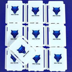 May include: White rectangular cases with a blue wolf head logo and the text "WOLF MOTION" are arranged on a blue background. The cases are stacked, with some slightly overlapping, creating a pattern. The wolf head is detailed.