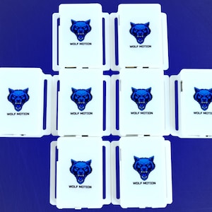 May include: Nine white rectangular objects with a blue wolf head logo and the text "WOLF MOTION" are arranged on a blue surface. The wolf head is a detailed illustration.