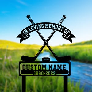 May include: Black metal memorial garden stake with crossed hockey sticks, a puck, and a banner reading "IN LOVING MEMORY OF." The bottom section has space for a custom name and the years 1960-2022.