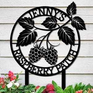 May include: Black metal sign with the text "JENNY'S RASPBERRY PATCH" in a circular design. The sign features two raspberries and leaves. The sign is mounted on a stake, suitable for a garden or yard.