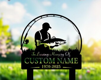 May include: Black metal garden stake featuring a silhouette of a fisherman holding a fish, framed by a fishing rod. The stake includes the text "In Loving Memory Of CUSTOM NAME 1970-2025". The background shows a blurred green lawn and blue sky.