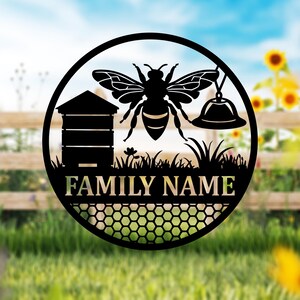 May include: Black metal bee-themed family sign. The design features a bee, beehive, and honeycomb pattern, with space for a family name. The sign is circular and suitable for outdoor or indoor display.