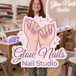 May include: A person holding a sign for "Glow Nails Nail Studio." The sign features a graphic of two hands with manicured nails, surrounded by stars. The studio's name is written in a cursive font. The background shows a nail salon.