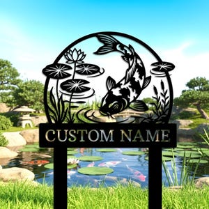 Puede incluir: Estaca de jardín de metal negro con un diseño de carpa koi y el texto "CUSTOM NAME". La carpa koi es negra y blanca, nadando en un estanque con nenúfares y una flor de loto. El fondo muestra un estanque con carpas koi.