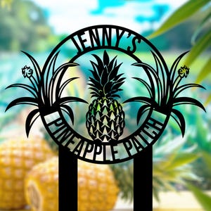 May include: Black metal sign with the text "JENNY'S PINEAPPLE PATCH" in a circular design. The sign features a pineapple in the center, surrounded by stylized leaves and flowers. The background is blurred, with visible pineapples and foliage.