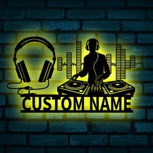 Może przedstawiać: Czarna sylwetka grafiki ściennej DJ-a ze słuchawkami, gramofonami i grafiką fali dźwiękowej. Tekst "CUSTOM NAME" jest wyświetlany poniżej. Grafika jest podświetlona żółtą poświatą na tle ceglanej ściany.