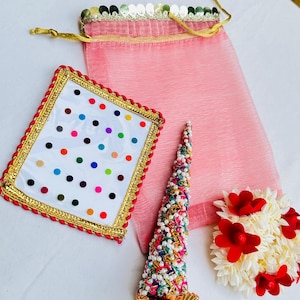 May include: A collection of decorative items including a pink drawstring bag, a white framed piece with colorful dots, a beaded cone-shaped ornament, and a floral hair accessory with red accents. The items are arranged on a white surface.
