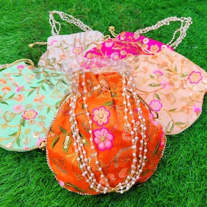 Puede incluir: Una variedad de bolsos con cordón bordados y coloridos. Los bolsos son de color naranja, rosa, verde menta y crema, con diseños florales y detalles de cuentas. Cada bolso tiene una cadena de cuentas.