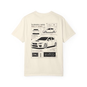 May include: A cream-coloured t-shirt with a black graphic of a Subaru WRX rally car. The design includes technical diagrams, the text "SUBARU WRX RALLY KING", and other automotive details. The shirt has a classic crew neck.