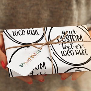 May include: A wrapped gift box with a white background and black circular designs. The box is tied with twine and has a tag that says "Pixel-Print". The box has the text "LOGO HERE" and "your CUSTOM Text or LOGO HERE".