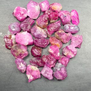 Peut inclure: Une collection de rubis bruts et non polis dans des nuances variées de rose vif et de magenta profond. Ces spécimens minéraux naturels présentent des formes irrégulières et dentelées ainsi que des textures cristallines, opaques et translucides.