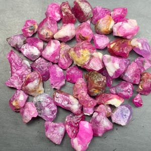 Peut inclure: Une collection de rubis bruts et non polis dans diverses nuances de rose vif et de magenta profond. Ces spécimens minéraux naturels présentent des formes irrégulières et dentelées avec des textures translucides à opaques.