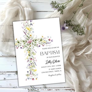 Op de afbeelding: Een witte doopuitnodigingskaart met een bloemenkruisontwerp. Het kruis is versierd met aquarelbloemen in roze, gele en paarse tinten. De kaart bevat de tekst "PLEASE JOIN US FOR THE BAPTISM OF OUR DAUGHTER Lilly Oliver".