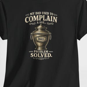 Könnte beinhalten: Schwarzes T-Shirt mit einem humorvollen Aufdruck. Das Design zeigt eine dekorative Urne mit dem Wort "DAD" und dem Text "MY DAD USED TO COMPLAIN A LOT... PROBLEM SOLVED."