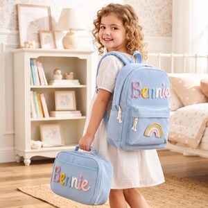 Può includere: Uno zaino e una borsa per il pranzo abbinata in velluto a coste azzurro. Entrambi gli articoli presentano il nome Bennie in lettere colorate, in rilievo e imbottite. Lo zaino include una piccola toppa arcobaleno e tiretti della cerniera bianchi.