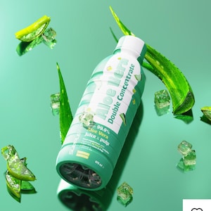 May include: A green bottle of Aloe Vera Double Concentrate with white text and accents. The bottle is surrounded by aloe vera leaves and ice cubes on a green surface. The bottle contains 675 ml of product.