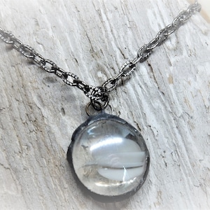 May include: A silver chain necklace with a round glass pendant. The pendant is clear and has a white swirl inside.
