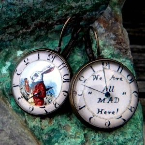 May include: A pair of bronze-colored dangle earrings with a white clock face. One earring features a white rabbit with a pocket watch, and the other earring features the text "We Are All MAD Here!"