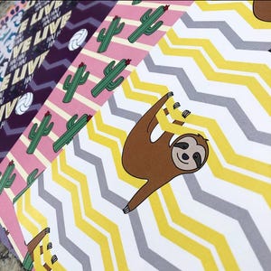 May include: A collection of patterned papers with various designs. One paper features a brown sloth hanging upside down. Other papers display cactus illustrations, chevron patterns, and text that reads "LIVE". The color palette includes pink, yellow, gray, and purple.