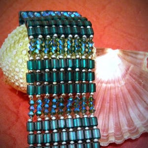 May include: A green and blue beaded bracelet with a geometric pattern. The bracelet is made with square and round beads.
