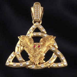May include: Gold pendant featuring a stylized bird within a Celtic knot design. The pendant is adorned with numerous small, clear gemstones and two red gemstones for the bird's eyes. The bail is also encrusted with gemstones. The background is black.