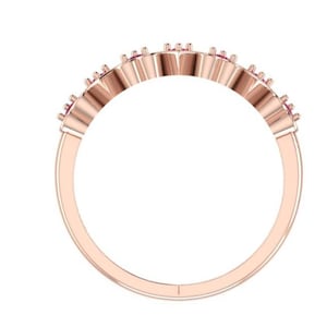 May include: Rose gold ring with a row of small, pink gemstones. The ring band is a smooth, polished metal. The gemstones are set in a delicate, repeating pattern along the top of the ring.