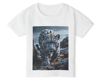 May include: White t-shirt featuring a detailed illustration of a snow leopard with blue eyes, walking on a rocky terrain. The leopard's fur is white with black spots. The background shows a cloudy sky and rocks.