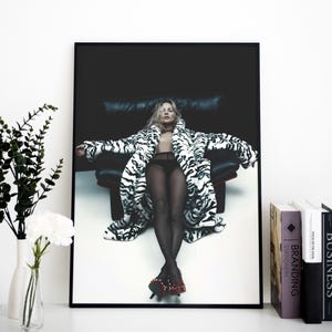 May include: A framed fashion photograph featuring a woman in a zebra-print coat, black lingerie, and red studded heels. The woman is seated in a black leather chair against a dark background. The photograph is displayed on a white surface.