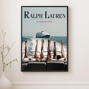 May include: A framed poster with the text "Ralph Lauren SUMMER 1998". The image shows legs raised on a boat, with a ferry in the background on a sunny day, over the sea.
