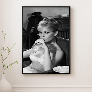 Puede incluir: Impresi&oacute;n enmarcada en blanco y negro de una mujer con sujetador blanco, bebiendo de un vaso. La imagen es una fotograf&iacute;a vintage, con la mujer sentada en una silla. Un plato est&aacute; sobre la mesa. La impresi&oacute;n se muestra en una pared blanca.